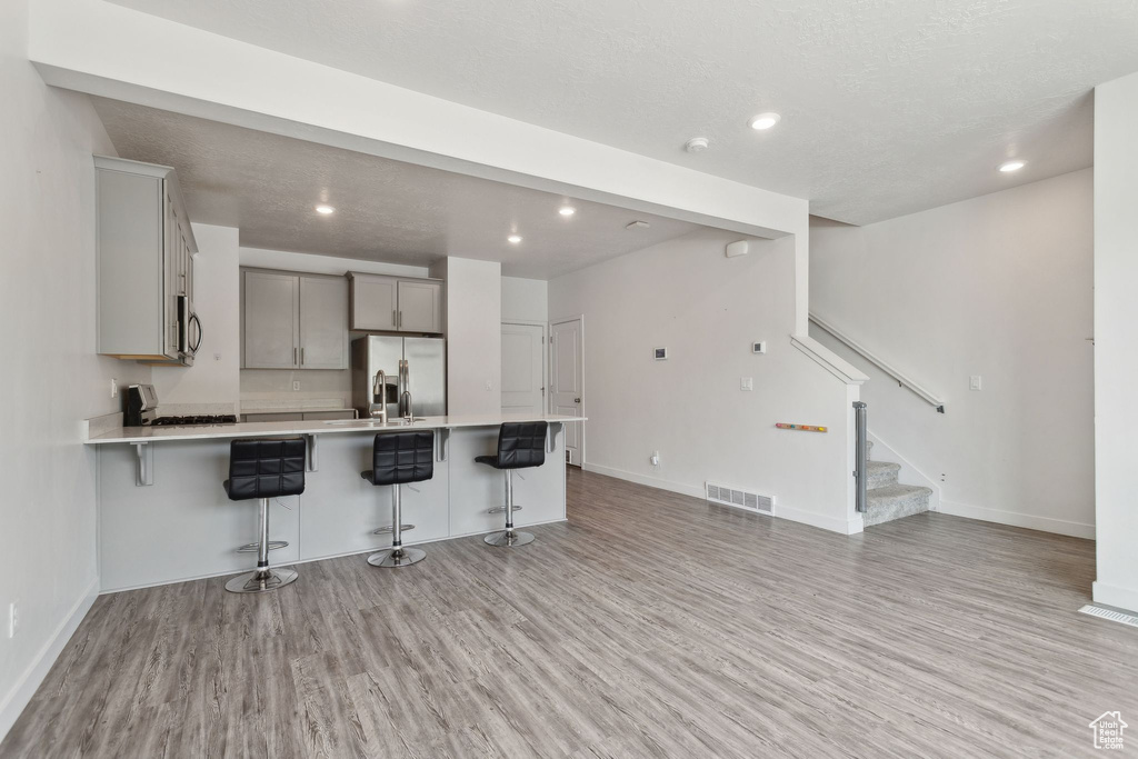 Kitchen featuring appliances with stainless steel finishes, light wood-type flooring, a kitchen breakfast bar, light countertops, and recessed lighting