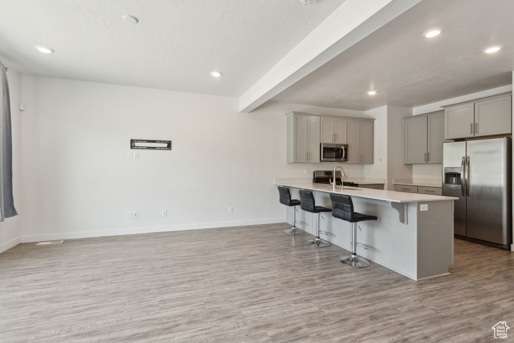 Kitchen with appliances with stainless steel finishes, gray cabinets, a breakfast bar area, light wood-type flooring, and light countertops