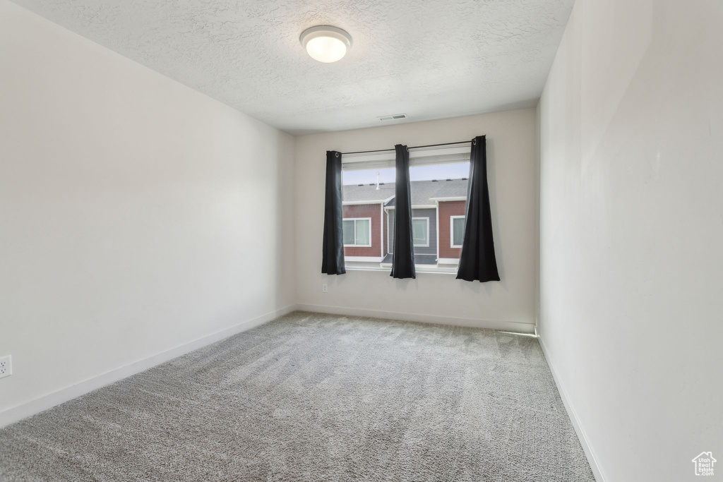 Carpeted empty room with a textured ceiling and baseboards