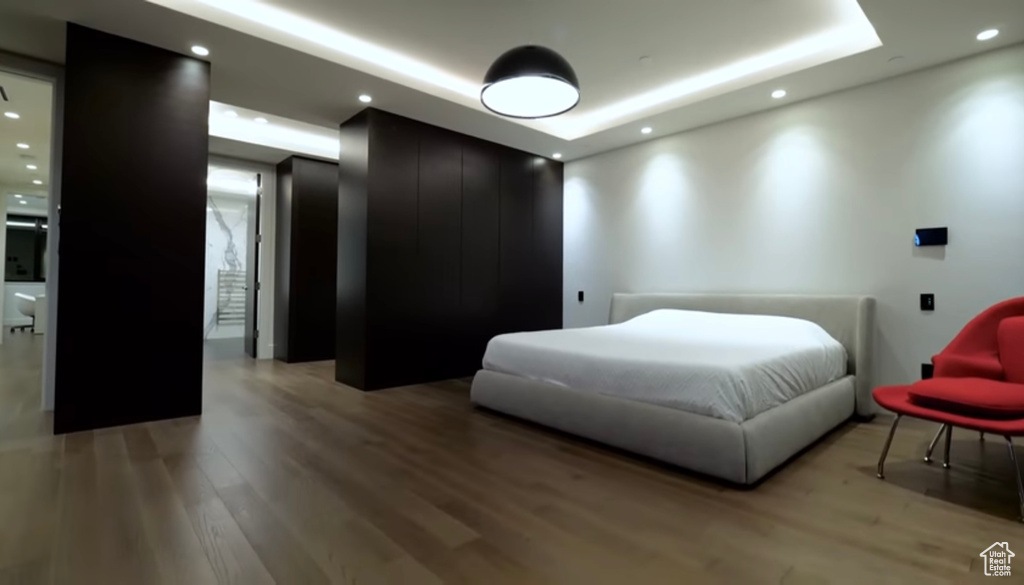 Bedroom with a tray ceiling, light wood-style floors, and recessed lighting