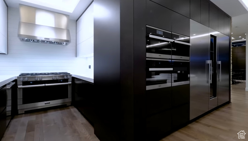 Kitchen featuring stainless steel stove, wall chimney exhaust hood, modern cabinets, light wood-style floors, and dark cabinetry