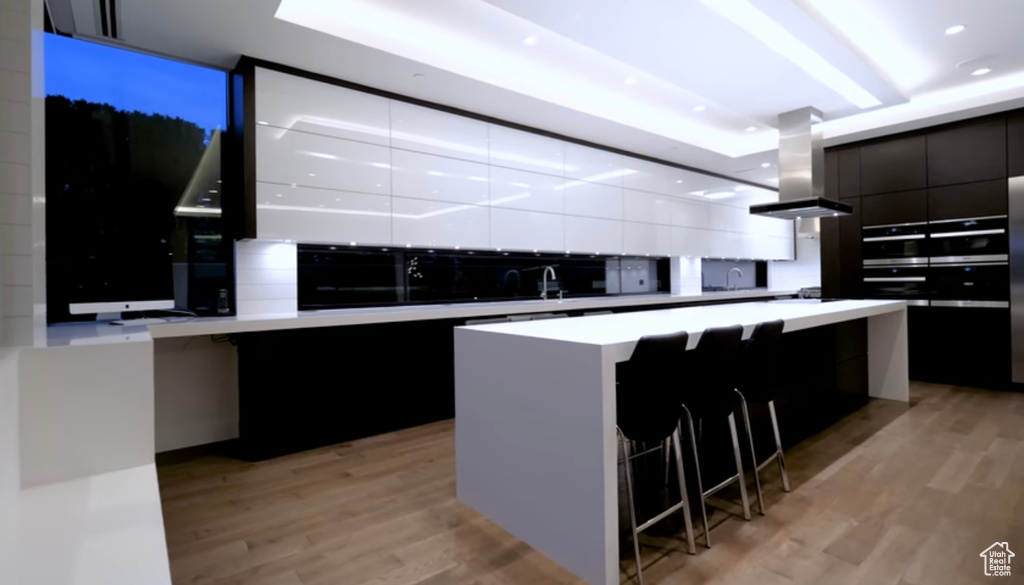 Kitchen with modern cabinets, exhaust hood, light wood-style floors, a kitchen island, and dark cabinets