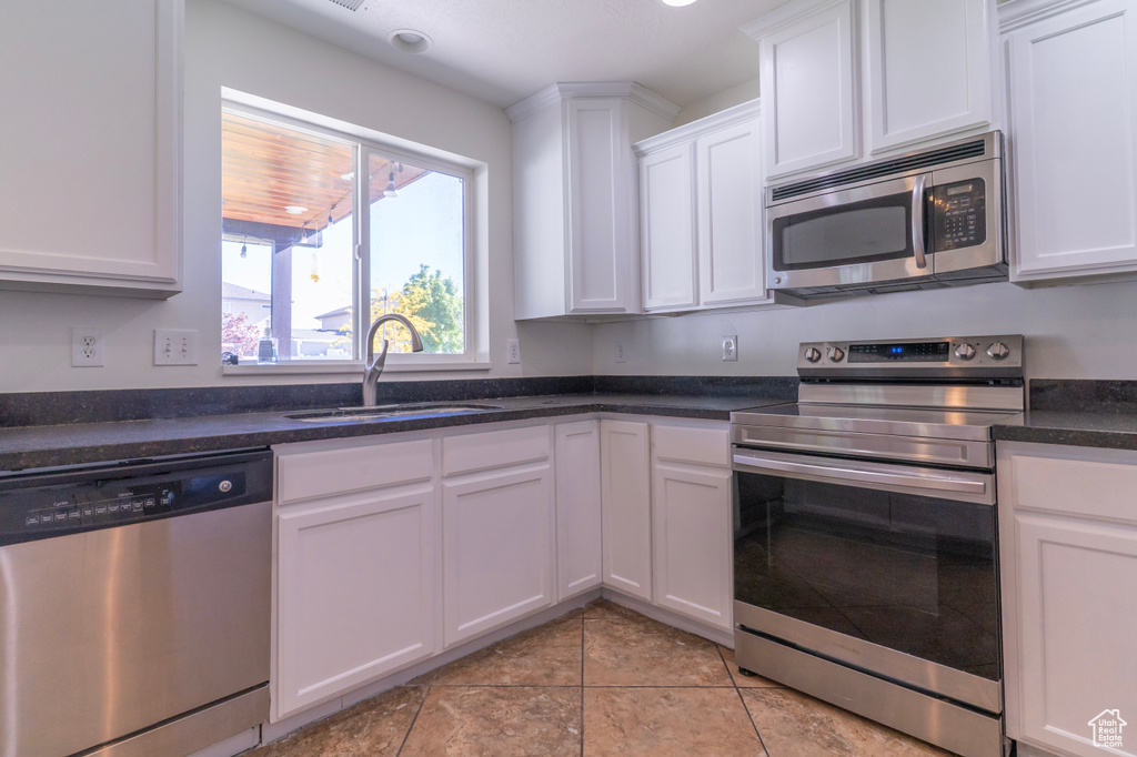 Kitchen with stainless steel appliances, a sink, white cabinets, and light tile patterned floors