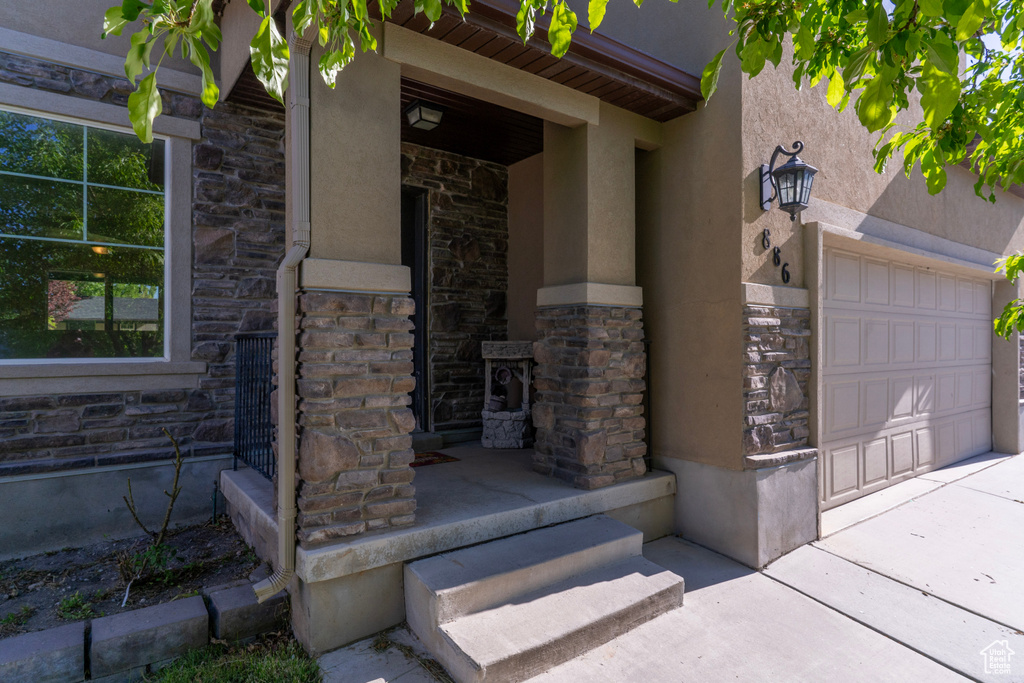 Entrance to property with stone siding, stucco siding, and a garage
