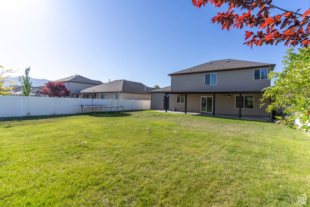 Back of property with a trampoline, a patio, and a shingled roof