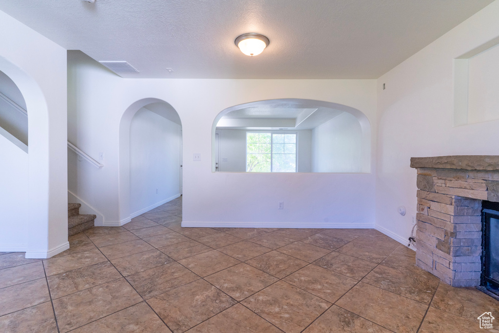 Unfurnished living room featuring a fireplace, a textured ceiling, stairs, baseboards, and tile patterned floors