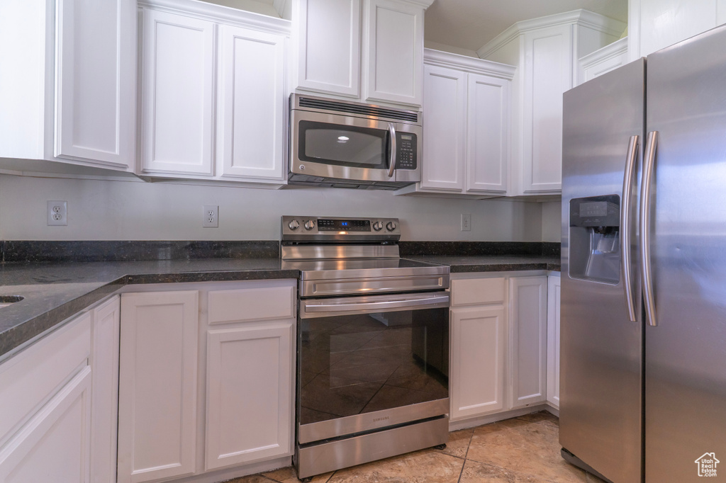 Kitchen with appliances with stainless steel finishes, white cabinetry, and dark stone counters