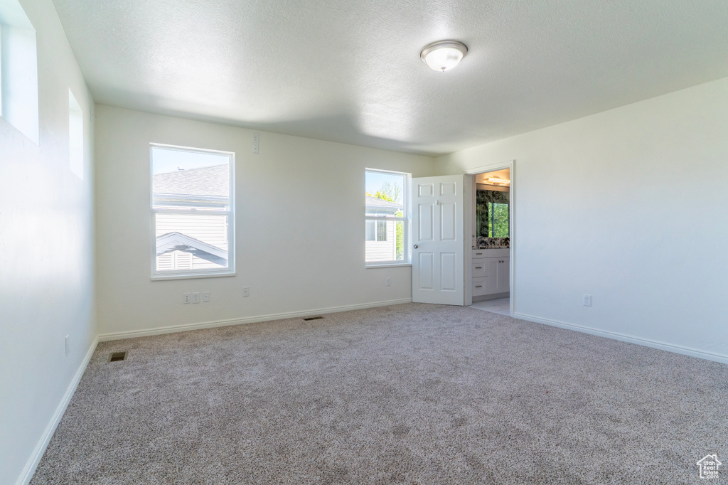 Empty room featuring light colored carpet, baseboards, and a textured ceiling