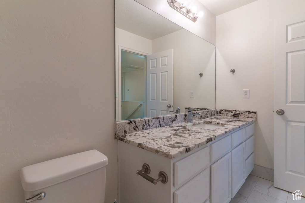 Half bathroom with marble finish floors, toilet, and vanity