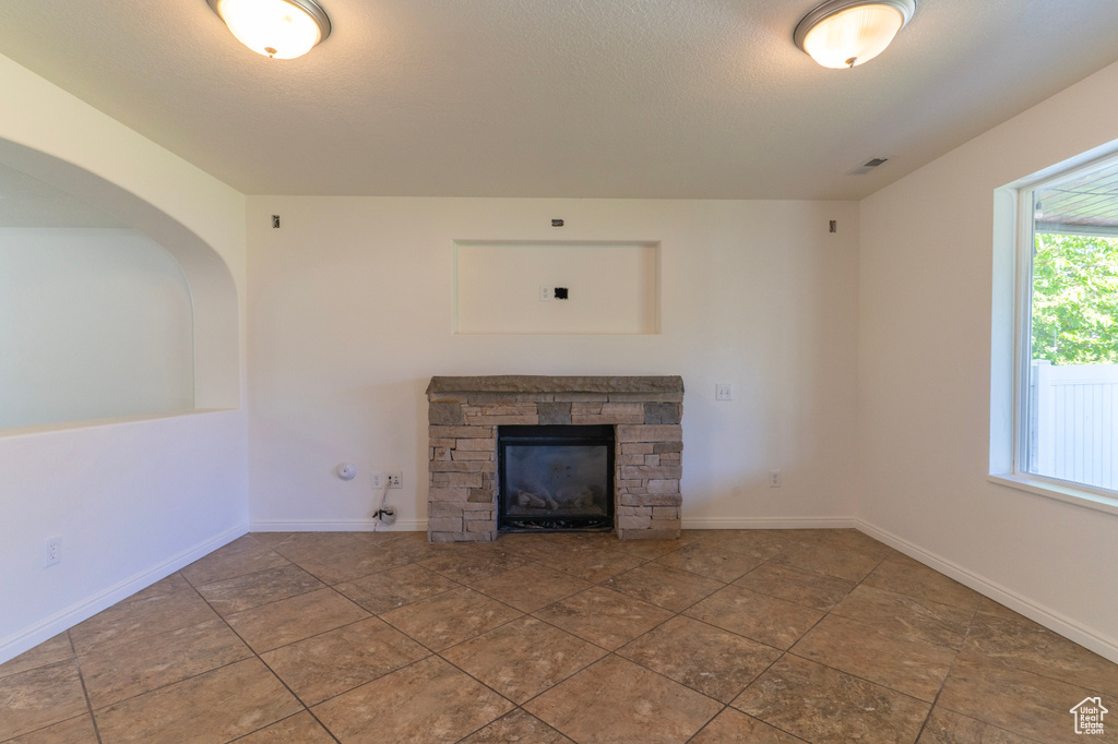 Unfurnished living room with a stone fireplace and baseboards