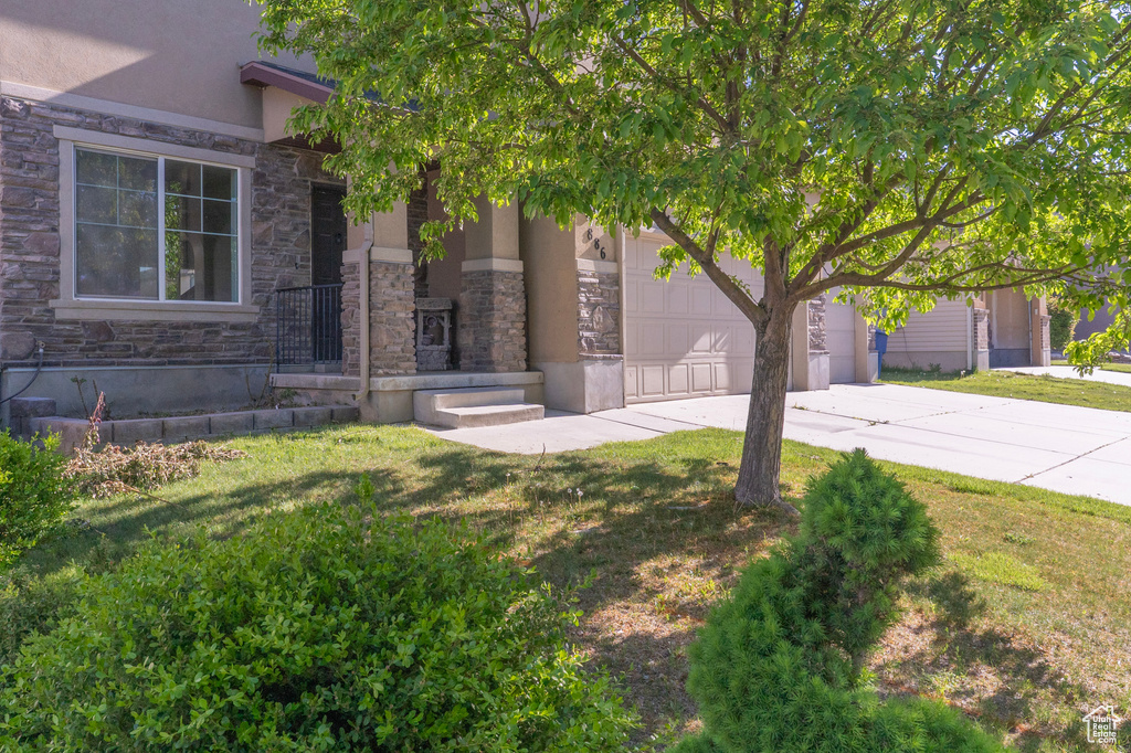 View of front of property featuring driveway, stucco siding, stone siding, and a front lawn
