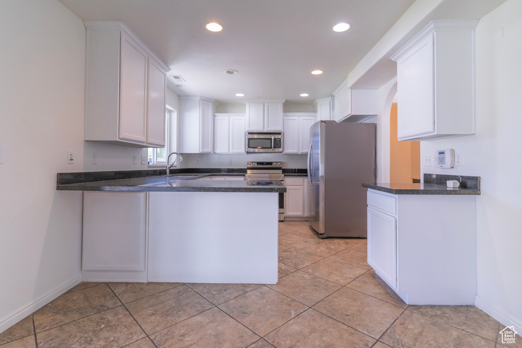 Kitchen with appliances with stainless steel finishes, a peninsula, white cabinets, recessed lighting, and baseboards