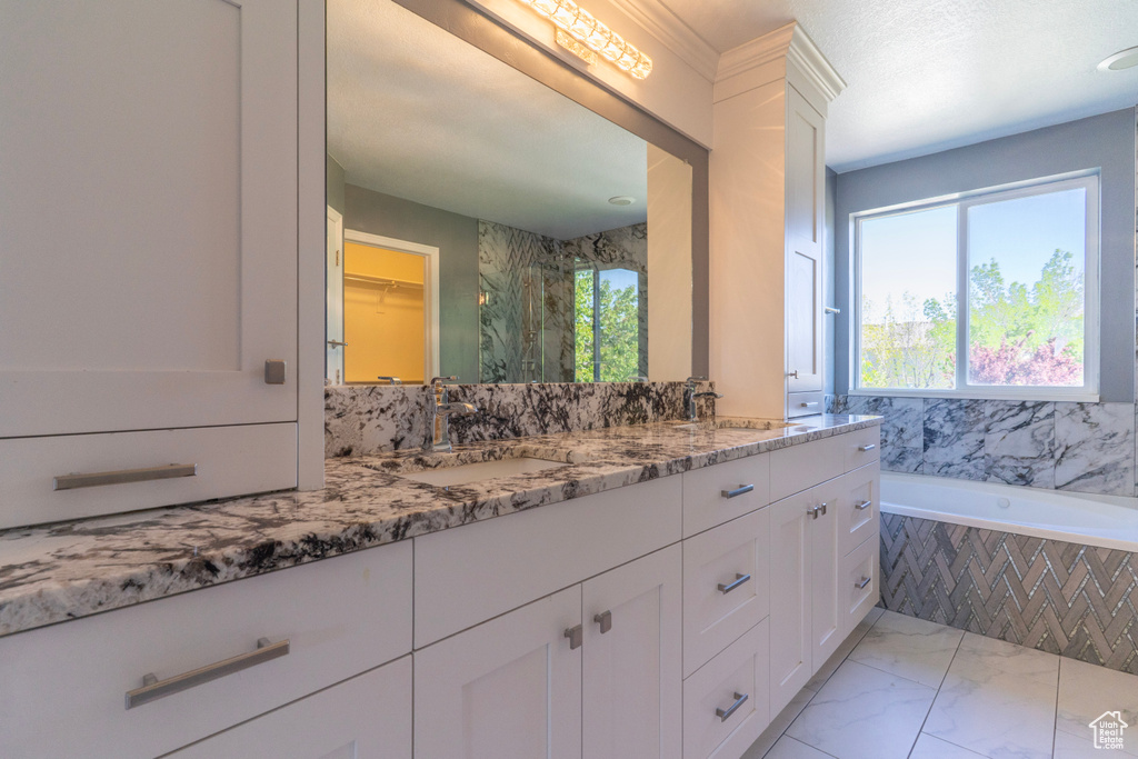 Bathroom with marble look tile flooring, double vanity, a bath, and a walk in closet