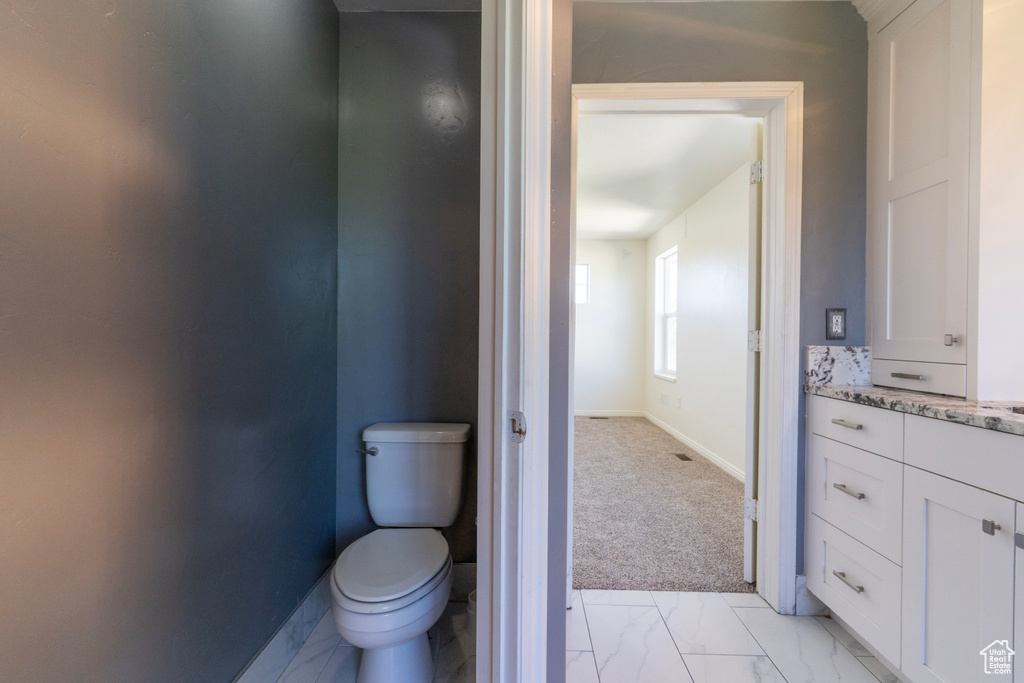 Bathroom featuring toilet, baseboards, marble finish floors, and vanity