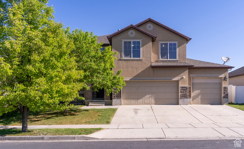 View of front facade with stucco siding, driveway, a garage, stone siding, and a front lawn