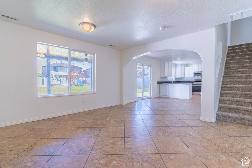 Unfurnished living room with arched walkways, stairs, light tile patterned floors, and a textured ceiling