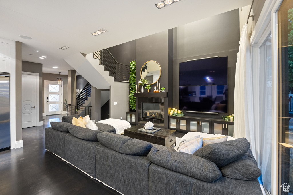 Living area featuring stairway, a glass covered fireplace, wood finished floors, baseboards, and recessed lighting