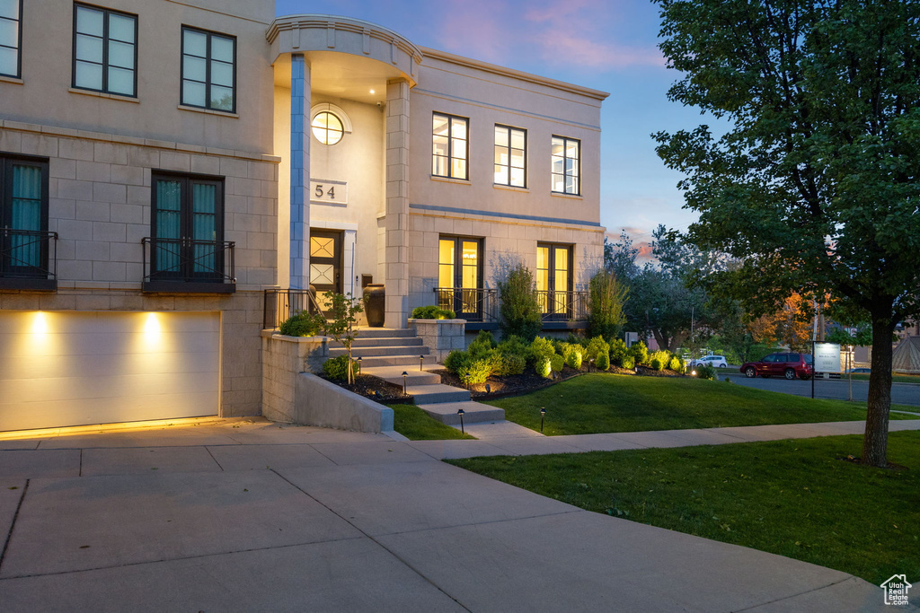 View of front of property featuring driveway, a front lawn, french doors, a garage, and stucco siding