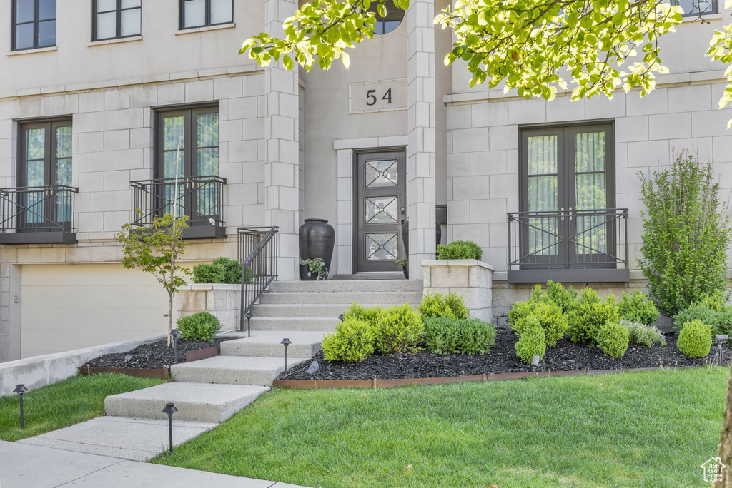 Doorway to property featuring french doors, an attached garage, a lawn, and stone siding