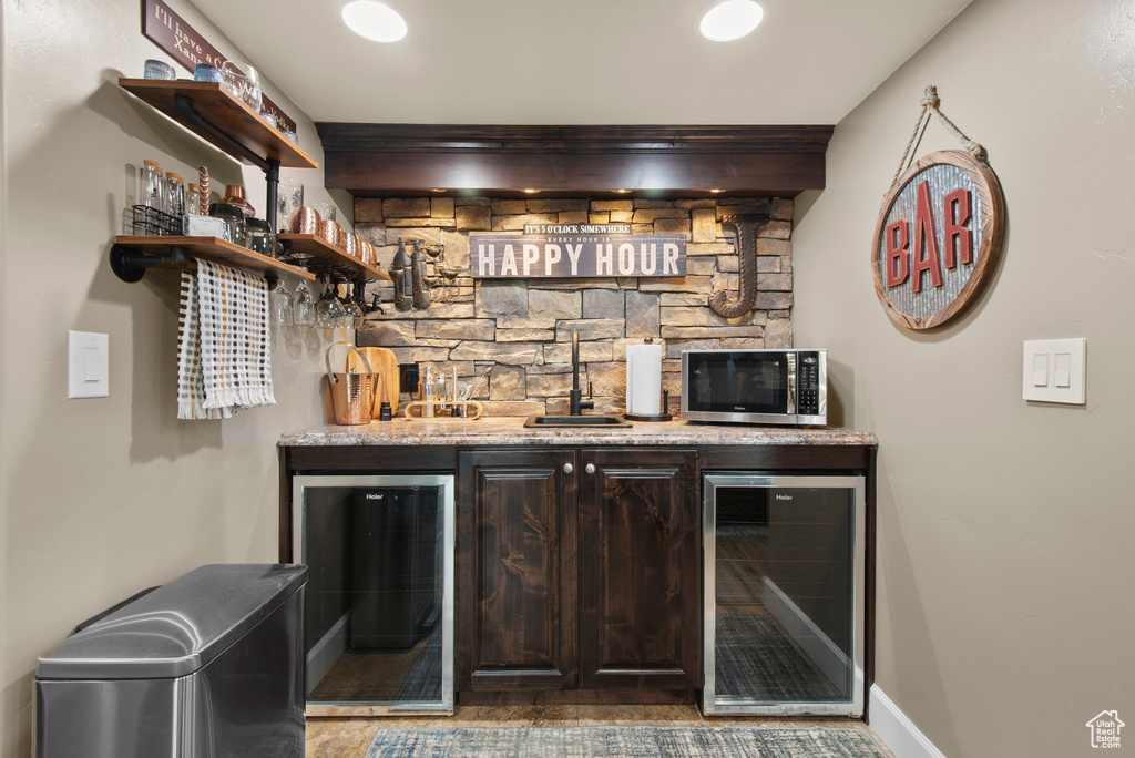 Indoor wet bar featuring wine cooler, stainless steel microwave, and baseboards