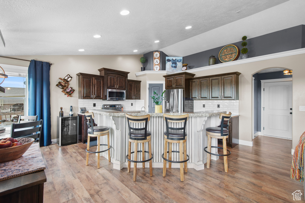 Kitchen with stainless steel appliances, lofted ceiling, tasteful backsplash, dark brown cabinetry, and a textured ceiling