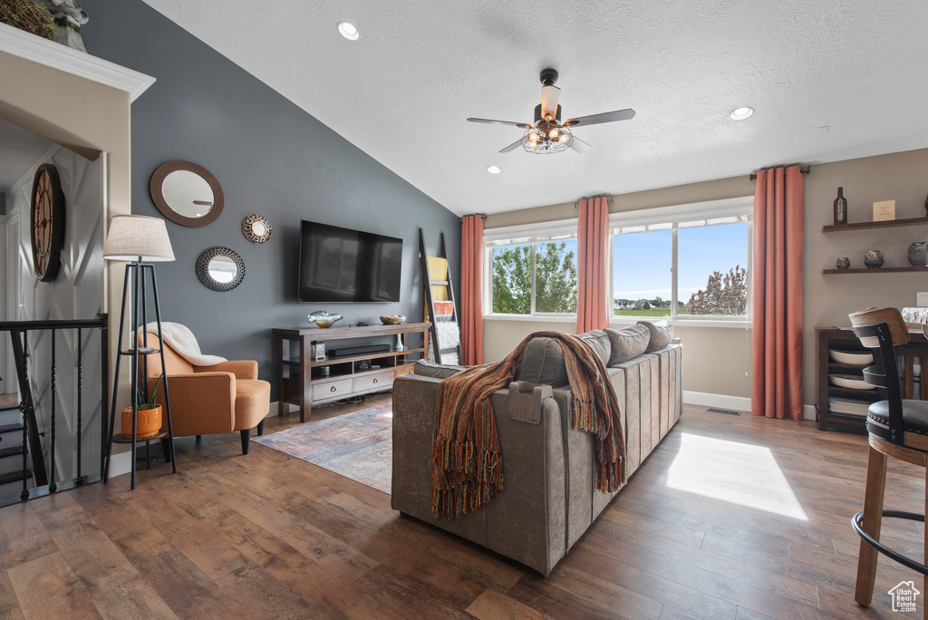 Living room with ceiling fan, vaulted ceiling, wood finished floors, recessed lighting, and a textured ceiling