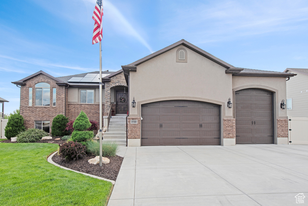 View of front of property with an attached garage, solar panels, a front lawn, brick siding, and driveway