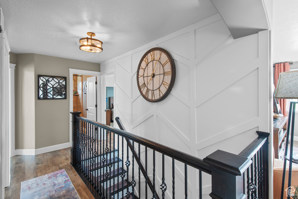 Corridor with an upstairs landing, wood finished floors, baseboards, and a textured ceiling