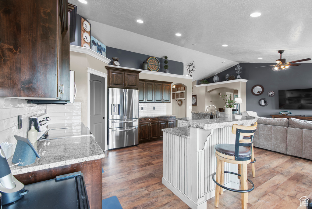 Kitchen featuring stainless steel refrigerator with ice dispenser, range, ceiling fan, open floor plan, and lofted ceiling