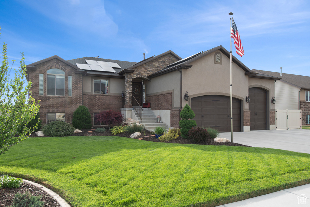 View of front of home with stucco siding, an attached garage, a front lawn, roof mounted solar panels, and concrete driveway