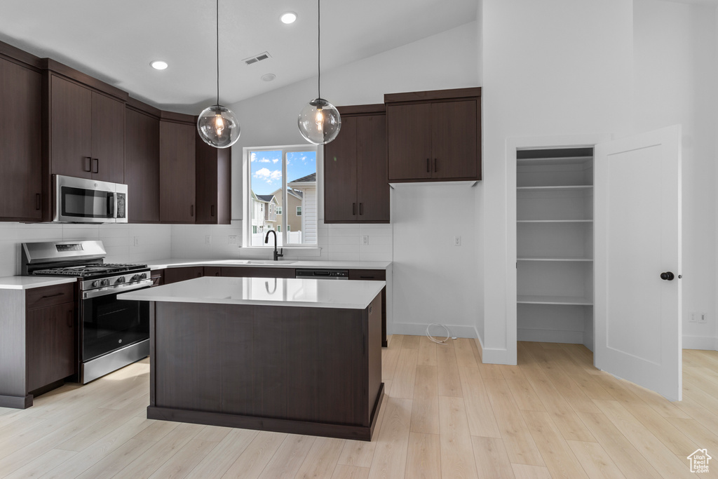 Kitchen featuring stainless steel appliances, dark brown cabinets, light countertops, light wood-type flooring, and recessed lighting