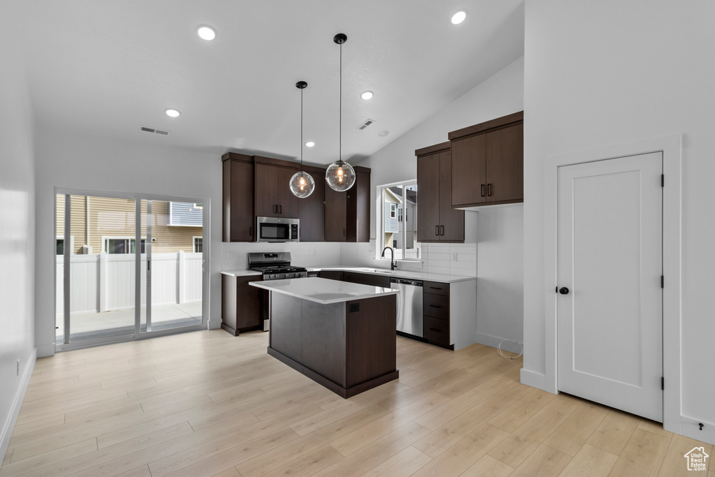 Kitchen with appliances with stainless steel finishes, dark brown cabinets, a kitchen island, backsplash, and light countertops