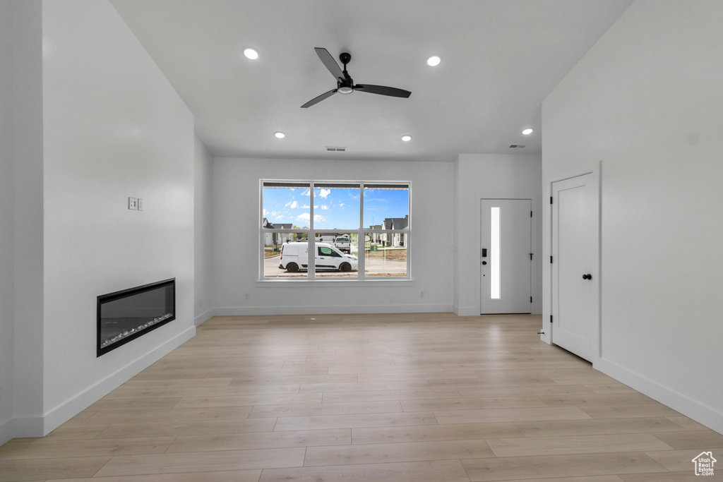 Unfurnished living room with a ceiling fan, a glass covered fireplace, recessed lighting, light wood-style flooring, and baseboards
