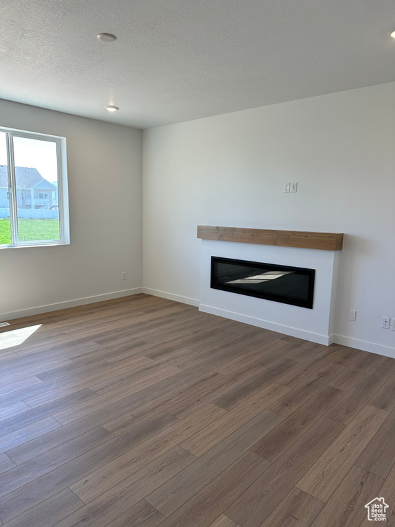 Unfurnished living room featuring a glass covered fireplace, wood finished floors, baseboards, a textured ceiling, and recessed lighting