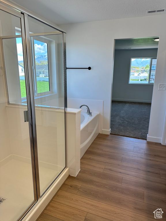 Bathroom with a garden tub, a stall shower, wood finished floors, and baseboards
