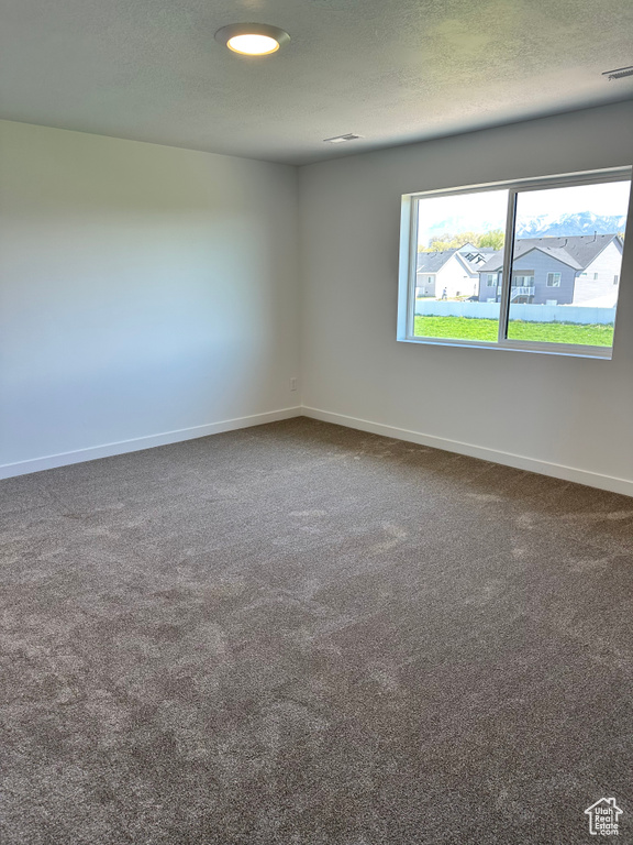 Empty room with baseboards, dark carpet, and a textured ceiling