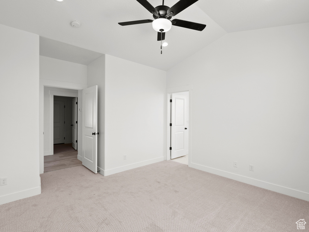 Empty room with vaulted ceiling, light carpet, ceiling fan, and a smoke detector