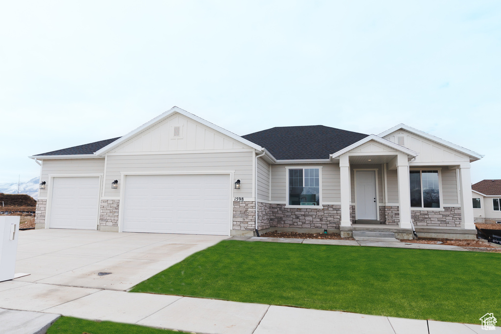 View of front of property with a garage, a front lawn, concrete driveway, and stone siding