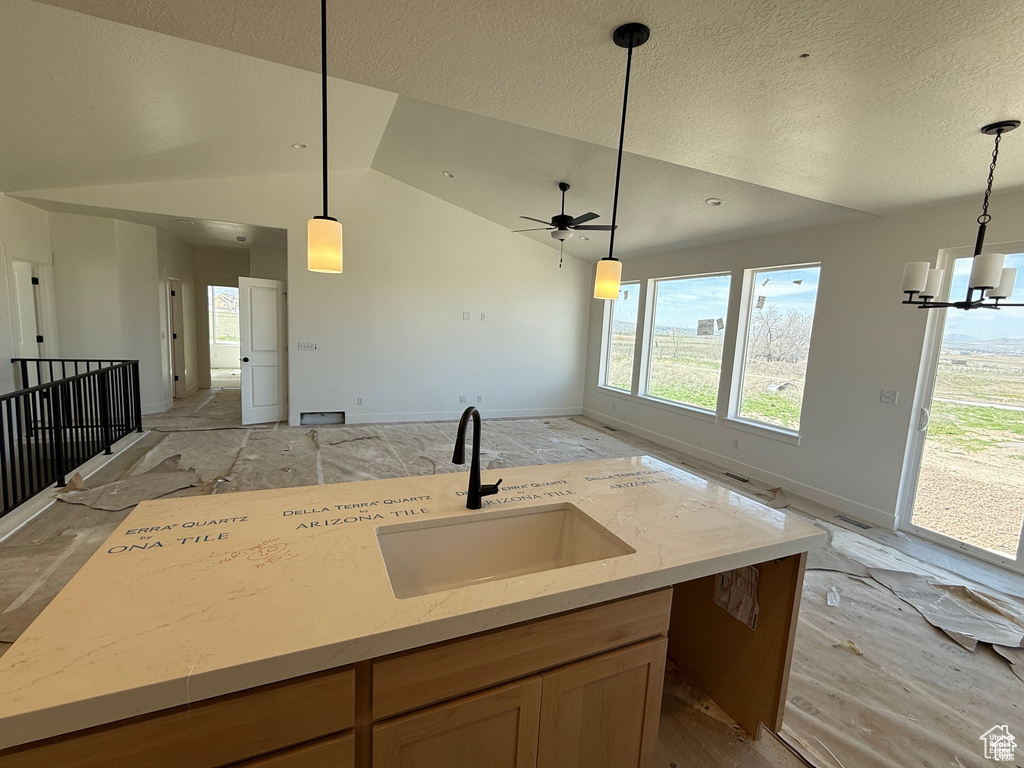 Kitchen featuring a sink, open floor plan, a textured ceiling, decorative light fixtures, and light stone counters