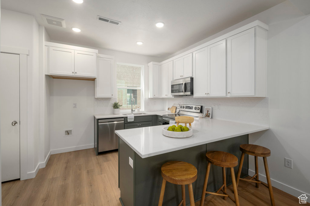Kitchen with stainless steel appliances, a sink, a peninsula, white cabinets, and recessed lighting