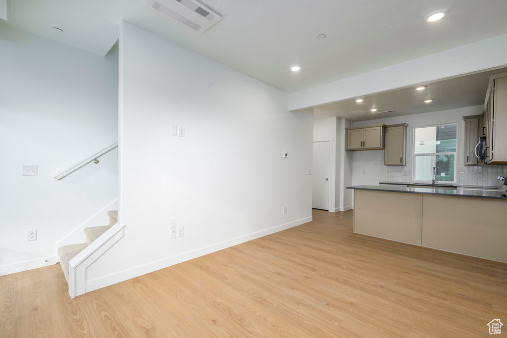 Unfurnished living room featuring light wood-type flooring, recessed lighting, stairs, baseboards, and a sink