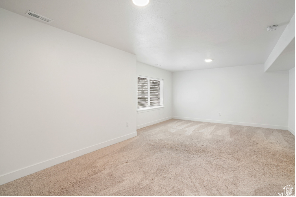 Empty room with light colored carpet, baseboards, and a smoke detector