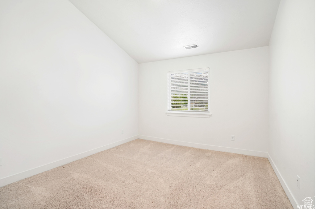 Spare room featuring light colored carpet, baseboards, and vaulted ceiling