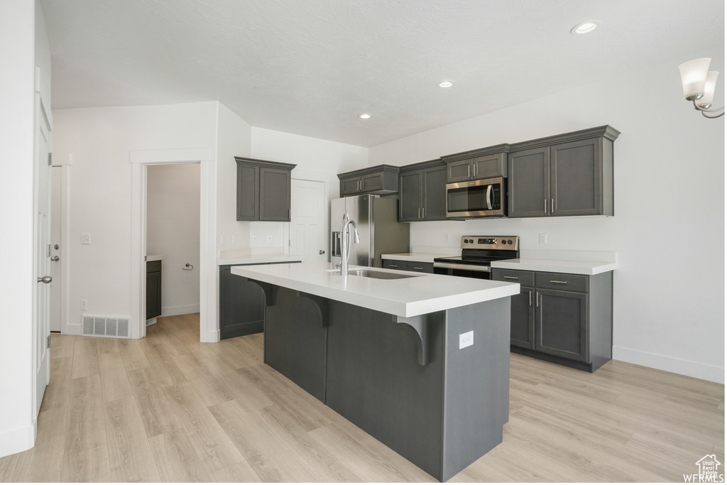 Kitchen featuring stainless steel appliances, a sink, baseboards, a center island with sink, and light wood-style floors
