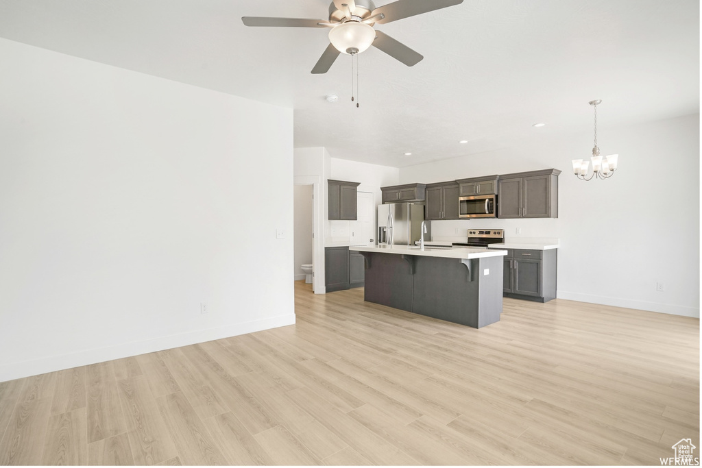 Kitchen featuring appliances with stainless steel finishes, a kitchen breakfast bar, a chandelier, light countertops, and light wood finished floors
