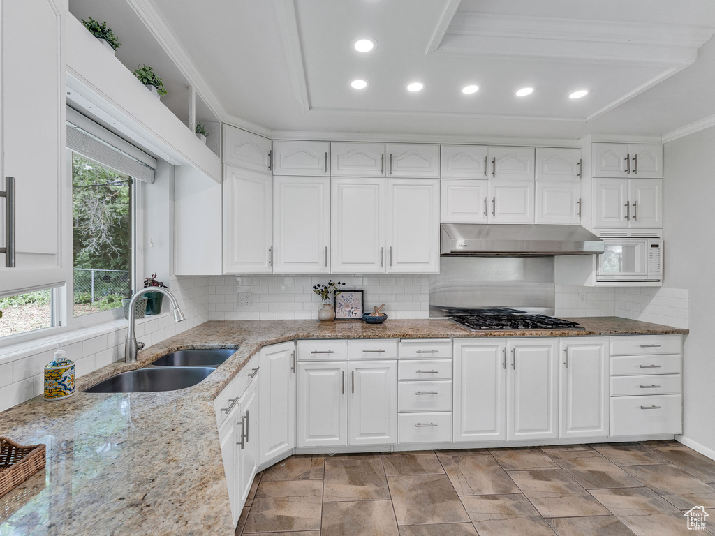 Kitchen featuring under cabinet range hood, a sink, stainless steel gas cooktop, recessed lighting, and tasteful backsplash