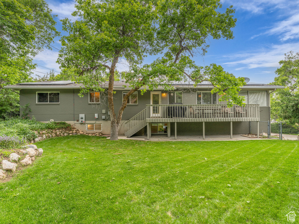 Rear view of property featuring stairs, a wooden deck, solar panels, and a patio