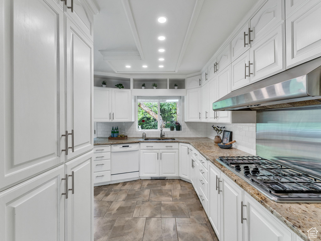 Kitchen with white dishwasher, under cabinet range hood, a sink, stainless steel gas stovetop, and decorative backsplash