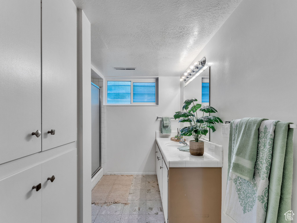 Full bathroom featuring a shower stall, vanity, a textured ceiling, and baseboards