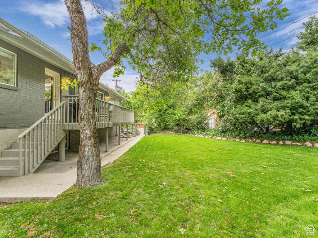 View of grassy yard with a patio area, a wooden deck, and stairs